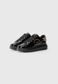 Glanzende zwarte lage sneakers met gouden oogjes, leopardenprint hielaccenten en gouden "Karl Lagerfeld Paris" branding aan de zijkanten.