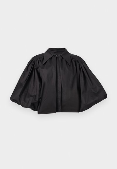 Veste noire courte avec des manches larges et volumineuses et un grand col pointu, présentée à plat sur un fond gris clair.