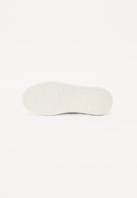 Biała podeszwa sneakerów z teksturowaną powierzchnią, z wzorem abstrakcyjnych kształtów i linii. Zaokrąglone krawędzie z lekkim podniesieniem w okolicy pięty.