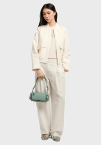 Giacca bomber cropped color crema, top in maglia, pantaloni beige a fantasia e bag verde. Texture liscia e design strutturato.