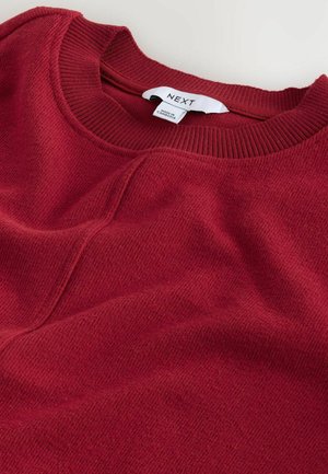 Roter Strickpullover mit geripptem Rundhalsausschnitt, weichem Material und einem dezenten diagonalen Muster. Er hat ein Etikett mit der Marke "NEXT."