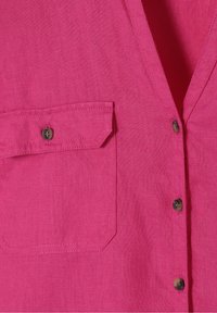 Chemise rose vif avec une poche poitrine équipée d'un rabat boutonné et une patte de boutonnage avant avec des boutons ronds foncés.