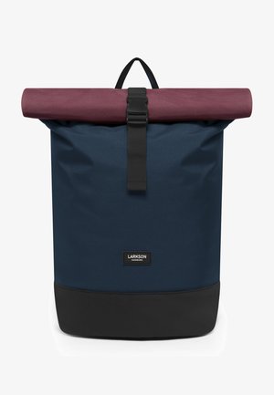 Tengerészkék roll-top hátizsák bordó fedéllel. Fekete pántos zárással rendelkezik, és fekete aljpanel található rajta. A címke jól láthatóan ki van téve.