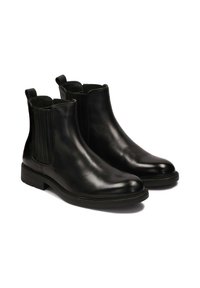 Botas Chelsea de cuero negro con paneles laterales elásticos, superficie lisa, punta redondeada y tacón bajo apilado. Doble tirador para facilitar el calzado.