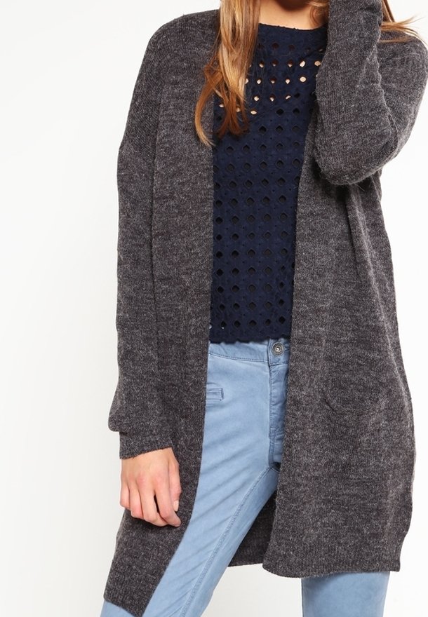 Mörkgrå cardigan med öppen framsida, långa ärmar och en mjuk textur, bärs över en marinblå topp med ett perforerat mönster.