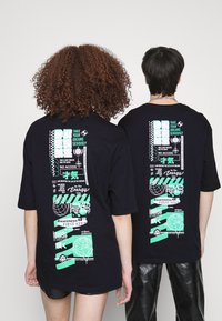 Černé oversize trička s zeleným grafickým textem a designem na zádech, s různými vzory a motivačními frázemi.
