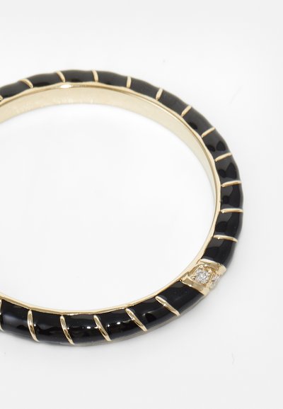 Črn bangle iz sijajnega materiala z zlatimi poudarki in strukturiranimi rebricami. Vsebuje tri majhne prozorne kamne. Ovalna oblika.