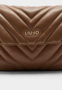 Braune, gesteppten Lederhandtasche mit Chevron-Muster, akzentuiert mit einem goldenen "LIUJO"-Logo. Glatte Textur und strukturierte Form.