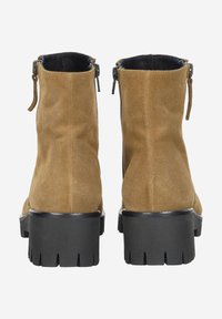 Pair of tan suede ankle boots with black chunky lug soles and back zippers, shown from the rear on a white background.