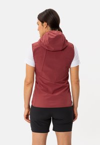 Gilet rosso senza maniche con cappuccio, realizzato in un materiale liscio e leggero. Presenta un design aderente e cuciture per una maggiore struttura. Pantaloni corti neri.