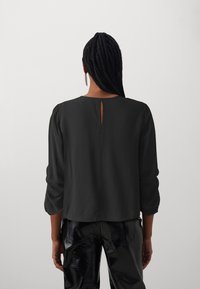 Black, lightweight blouse with three-quarter sleeves and a keyhole back detail, paired with shiny black, textured pants.
