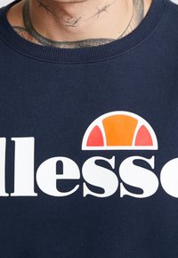 Sudadera azul marino con cuello redondo, que presenta un gran logo blanco y un gráfico colorido de un semicírculo en naranja y rojo.