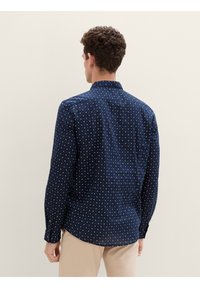 Marineblaue Hemdjacke mit einem gemusterten Design. Verziert mit kleinen weißen Sternen, langen Ärmeln und einem klassischen Kragen. Glatte Stofftextur.
