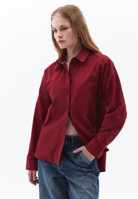 Rotes Hemd mit Knopfleiste und Kragen, lang�ärmlig und mit lockerer Passform, kombiniert mit hellblauen Jeans. Glatte Stofftextur.