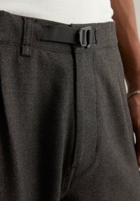 Dark gray trousers made of textured fabric, featuring a black adjustable belt and front pleats. Includes belt loops and subtle stitching details.