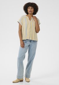 Flerfärgad kortärmad skjorta i gula och ljusblå ränder, med knäppning och avslappnad passform, kombinerad med högmidjade ljusa jeans.