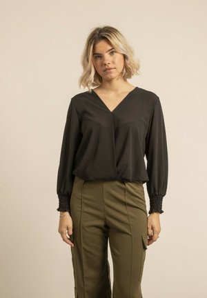 Blouse noire à manches longues avec un col en V, dotée de poignets smockés ; associée à un pantalon taille haute vert olive avec des poches cargo.