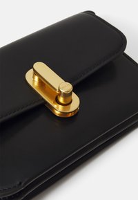 Clutch in pelle nera con hardware dorato, caratterizzato da un distintivo fermaglio ovale e linee pulite. Texture liscia con chiusura a pattina.