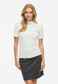 Vit texturerad blus med korta ärmar och en scalloped nacke, i kombination med en svart denimkjol. Enkel, figursydd design.