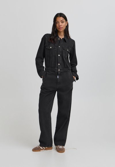 Melnā denima kombinezons ar apkakli, priekšējiem pogām, krūšu kabatām un brīvu piegriezumu ar sānu kabatām. Pabeigts ar sašaurinātu kāju.