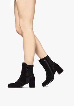 Bottes de cheville en suède noir avec un talon bloc, dotées d'une fermeture éclair sur le côté et de coutures contrastantes, au design élégant et à la texture douce.