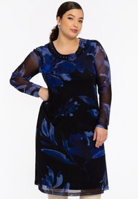 Langärmliges Kleid in Schwarz mit blauen Blumenmustern, mit einem runden Ausschnitt, der mit dekorativen Perlen verziert ist. Leichter, fließender Stoff.