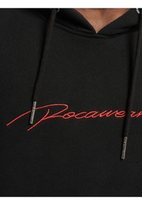 Fekete kapucnis pulóver, piros hímzett "Rocawear" felirattal. Állítható fekete zsinórokkal, fémből készült végződésekkel. Sima szövettextúra.