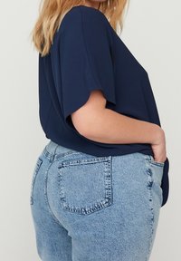 Maglietta blu navy, comoda e svasata con maniche corte, abbinata a pantaloni corti di denim azzurri a vita alta con tasche posteriori e una texture morbida.