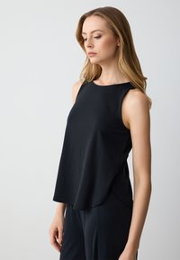 Top senza maniche nero con scollatura rotonda, realizzato in tessuto morbido e leggero. Presenta una vestibilità ampia e un orlo curvo.