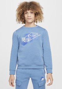 Sudadera azul Nike con cuello redondo, mangas largas y diseño de logo frontal que presenta acentos en degradé y puños de canalé, combinada con pantalones a juego.