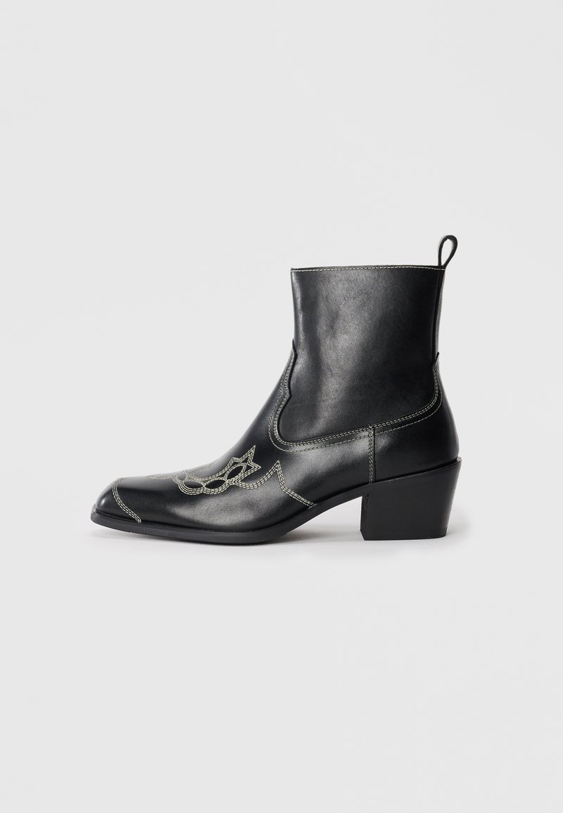 Botines de cuero negro hasta el tobillo con punta cuadrada, costuras decorativas y un tacón bajo en bloque. Incluyen una lengüeta para facilitar su colocación.