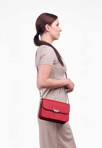 Červená kožená crossbody taška se zlatým zapínáním, obdélníkového tvaru, hladkým povrchem a řetězovým popruhem. Nošena ve výšce ramene.