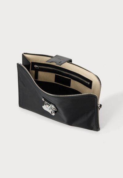 Pochette en cuir noir avec fermoir argenté, intérieur en tissu beige et poche intérieure zippée, présentée ouverte sur un fond uni.