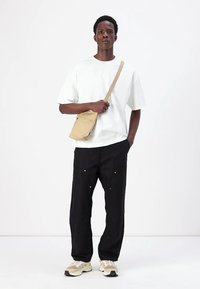 White short-sleeve t-shirt, black loose-fit pants, beige crossbody bag, and beige sneakers, standing on a white background.