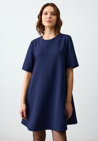 Abito blu navy con maniche corte, vestibilità comoda, scollatura tonda e una leggera forma a trapezio. Realizzato in tessuto liscio senza motivi visibili.