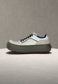 Κοντό αθλητικό παπούτσι με στρωματοποιημένο λευκό και μπεζ επάνω μέρος, μαύρα κορδόνια, μπλε επένδυση γιακά και παχύ παπούτσι με σκούρα γκρι σόλα πλατφόρμας.