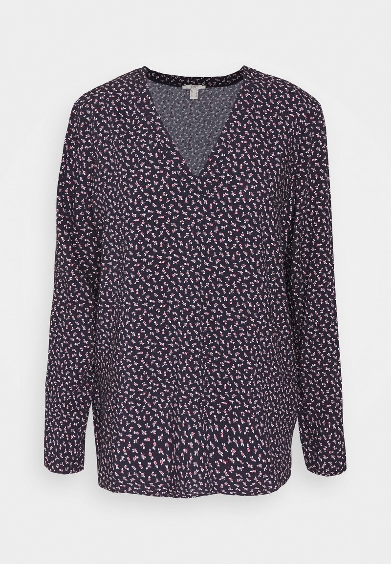 Blouse noire à manches longues avec petit motif floral rose et blanc et col en V sur fond uni.