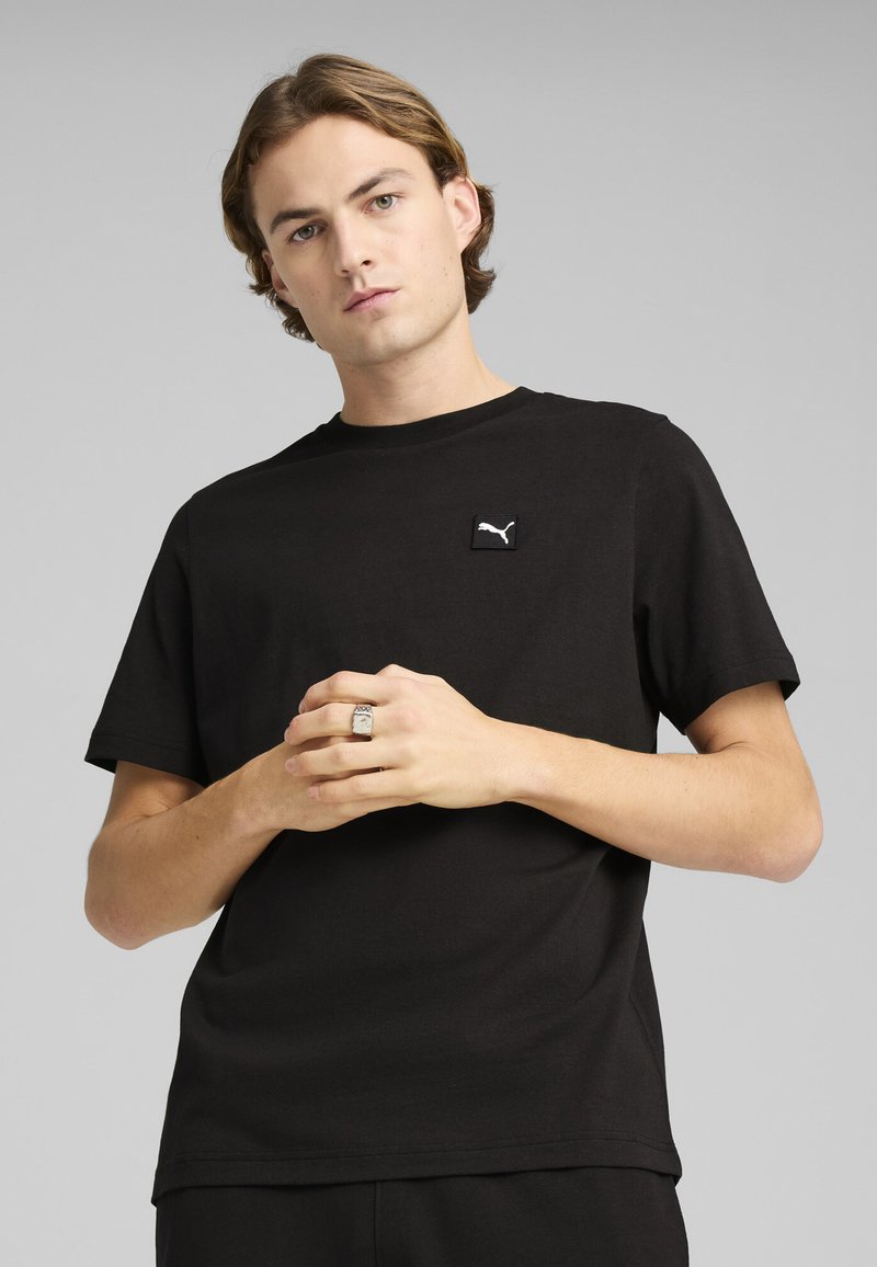 Black cotton T-shirt featuring a small white Puma logo on the upper left. Smooth texture and classic crew neck design.