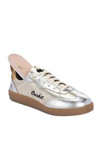 Sneaker metallic argento con lacci crema, un accento sul tallone color beige e un logo ricamato nero. Presenta una suola in gomma testurizzata e una soletta imbottita.