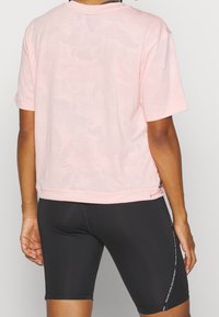Light pink short-sleeve T-shirt with a subtle floral pattern, round neckline, and a side zipper detail. Paired with black bike shorts.
