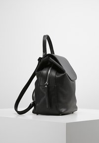 Svart läderryggsäck med en texturerad yta, ett lockstängning, en zip-försluten framficka och en justerbar rem.