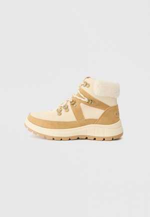 Beige og tan vandrestøvler med en tekstureret nubuck-overdel, fleecekrave og en kraftig gummisål. Har metaløjer og snørebånd.