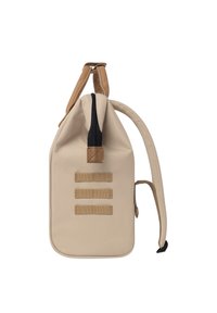 Sac à dos en tissu beige avec un design à rabat, fermeture éclair noire, bretelles beiges et trois boucles en toile horizontales pour attacher des accessoires.