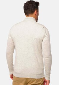 Pull en tricot gris clair avec un col haut, des poignets et un ourlet côtelés. Présente une finition texturée avec un motif subtil.
