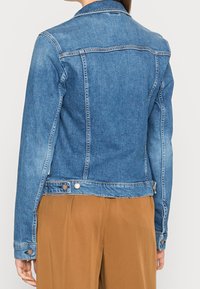 Jasnoniebieska kurtka dżinsowa z klasycznym kołnierzem, długimi rękawami i zapięciem na guziki przy mankietach oraz u dołu. Widok z tyłu.