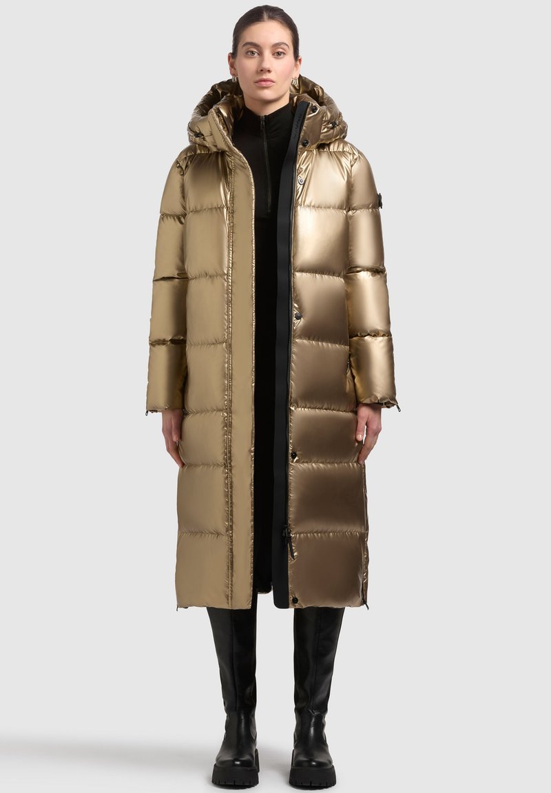 Die goldene Puffjacke verfügt über eine Kapuze, ein gestepptes Design und einen langen Schnitt. Glattes, glänzendes Material mit einem schwarzen Reißverschluss und Akzenten an den Bündchen.
