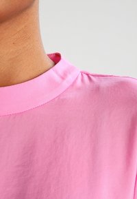 Top rosa a maniche corte con scollatura rotonda, texture liscia e leggero lucido. Presenta cuciture precise lungo il colletto.