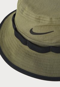 Olive green bucket hat with a black Nike logo. Features a textured fabric, a wavy black band, and a wide brim for sun protection.