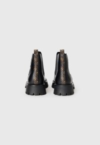 Une paire de bottines noires en cuir avec des semelles épaisses et des poignées en cuir avec des motifs logo marron, vues de l'arrière sur un fond blanc.