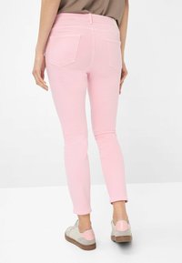 Jeans skinny in denim rosa chiaro con vita media, dotati di due tasche posteriori, abbinati a sneakers beige e rosa.